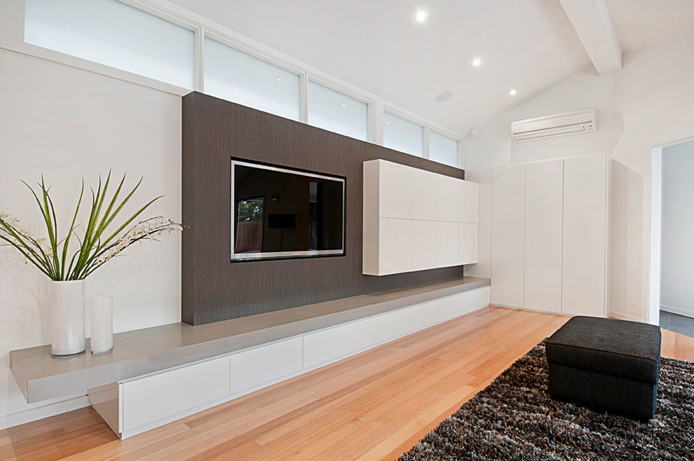 Modelo de cine en casa abierto moderno con paredes blancas, suelo de madera clara y televisor colgado en la pared