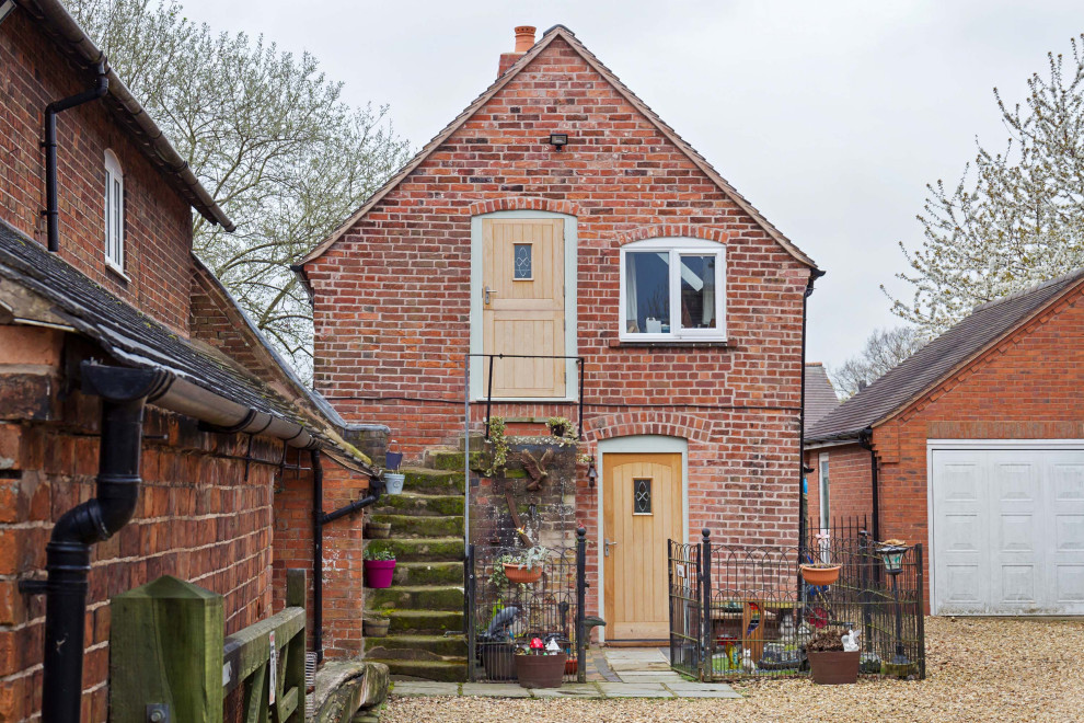 На фото: маленький, двухэтажный, кирпичный, красный мини дом в стиле рустика с двускатной крышей и черепичной крышей для на участке и в саду