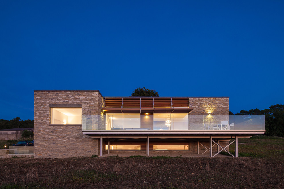 На фото: двухэтажный, бежевый дом в современном стиле с облицовкой из камня и плоской крышей с