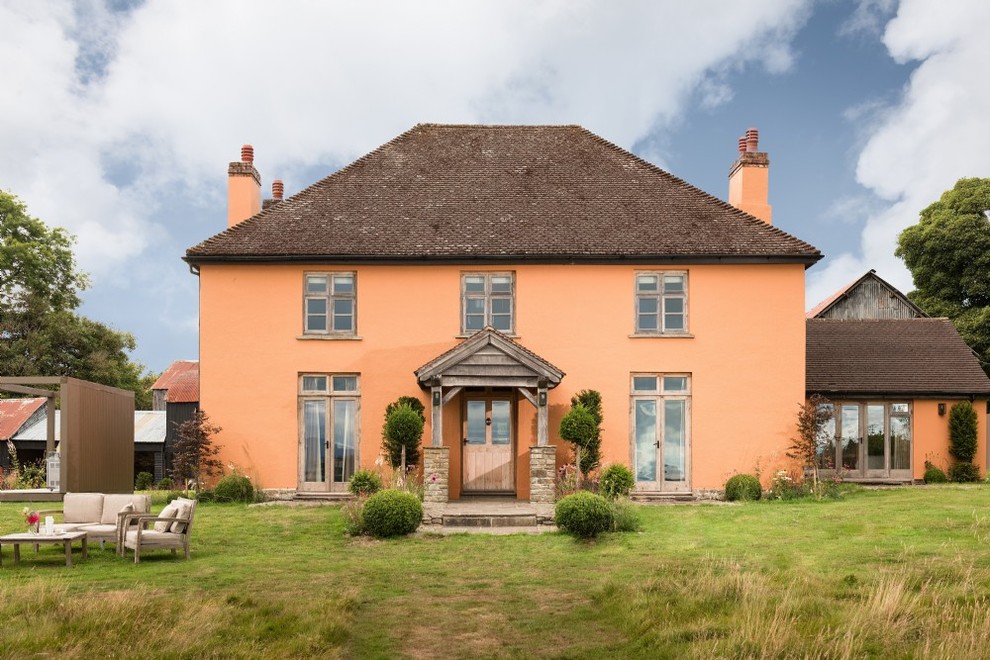 Пример оригинального дизайна: большой, трехэтажный, оранжевый частный загородный дом в стиле кантри с облицовкой из цементной штукатурки, вальмовой крышей и крышей из гибкой черепицы