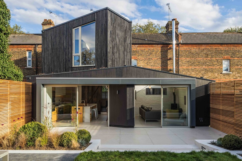 Photo of a black traditional split-level detached house in London with wood cladding and a pitched roof.