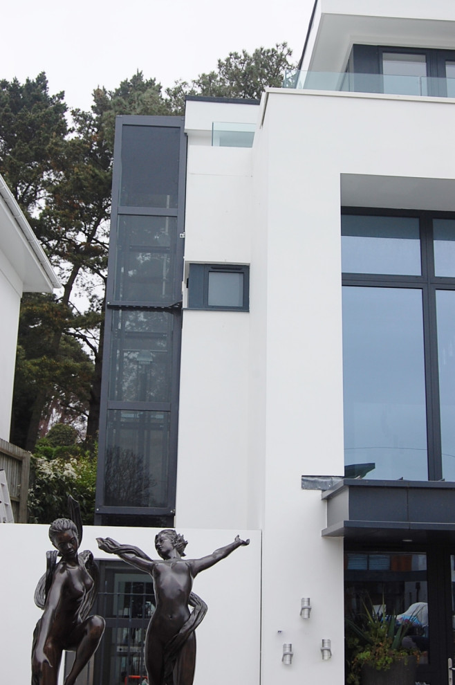 Mittelgroßes, Dreistöckiges Modernes Einfamilienhaus mit Glasfassade, weißer Fassadenfarbe, Flachdach und Blechdach in Dorset