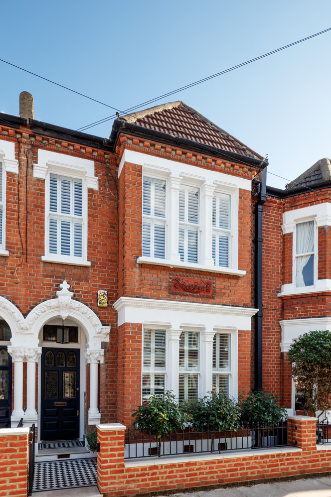 This is an example of a large and red traditional brick terraced house in London with three floors, a pitched roof and a tiled roof.