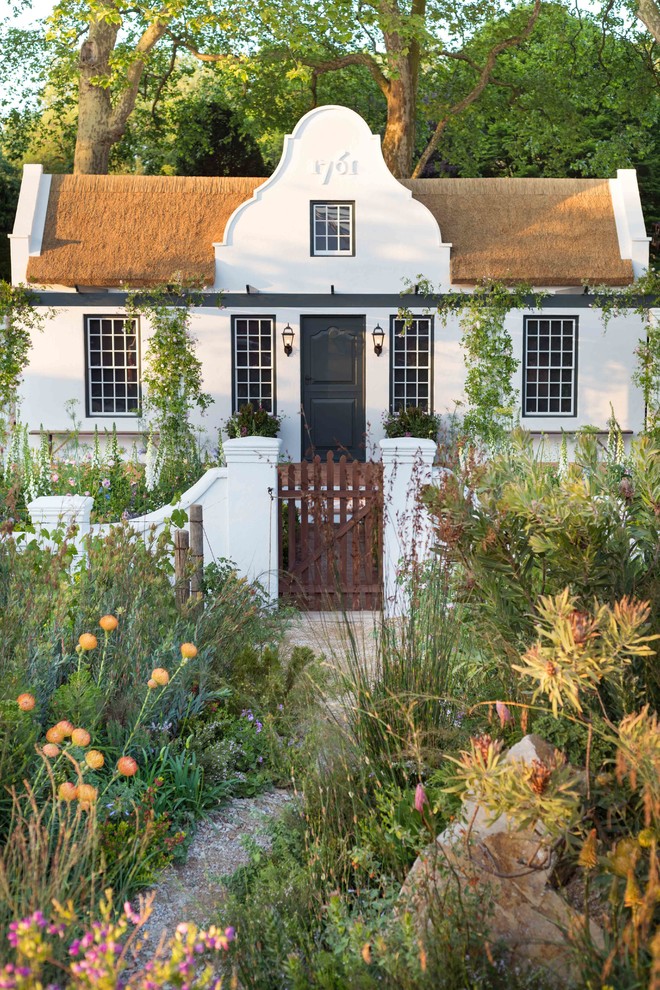 На фото: белый, маленький, двухэтажный частный загородный дом в стиле кантри с двускатной крышей для на участке и в саду