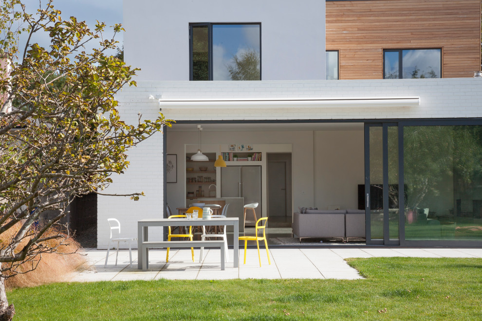 Cette image montre une façade de maison blanche design en brique de taille moyenne et à un étage avec un toit plat et un toit végétal.