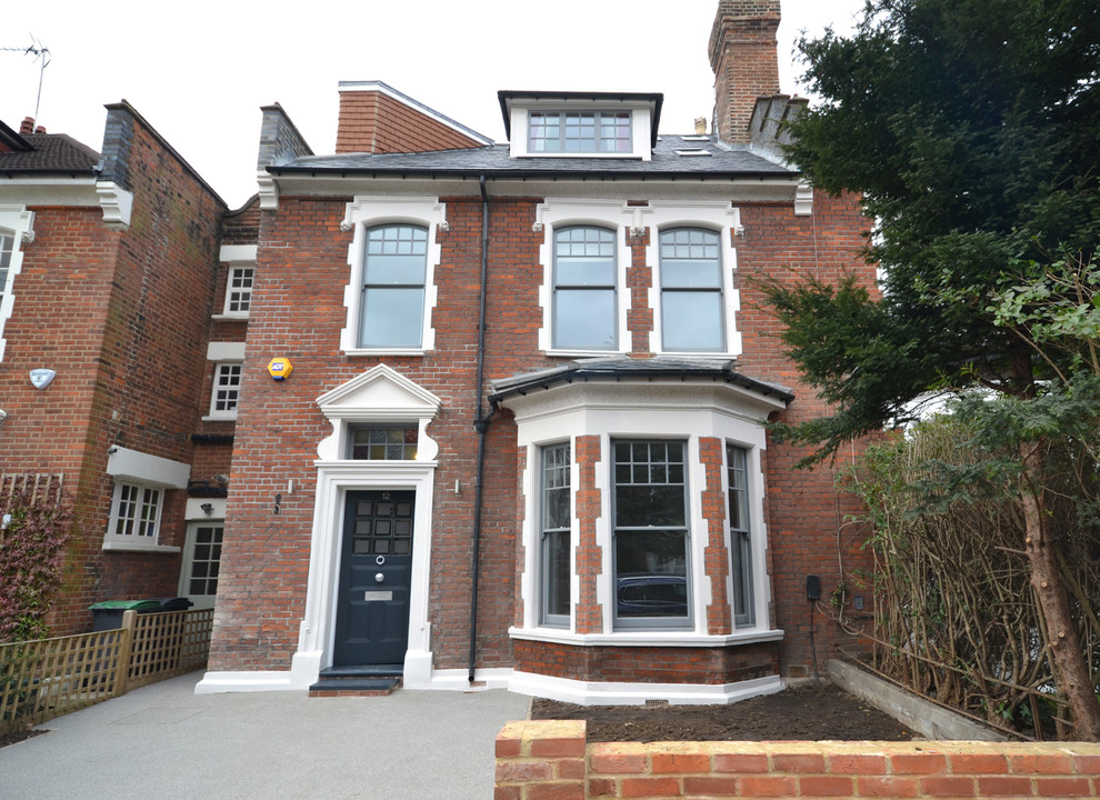 This is an example of a medium sized and red contemporary brick house exterior in London with three floors and a hip roof.