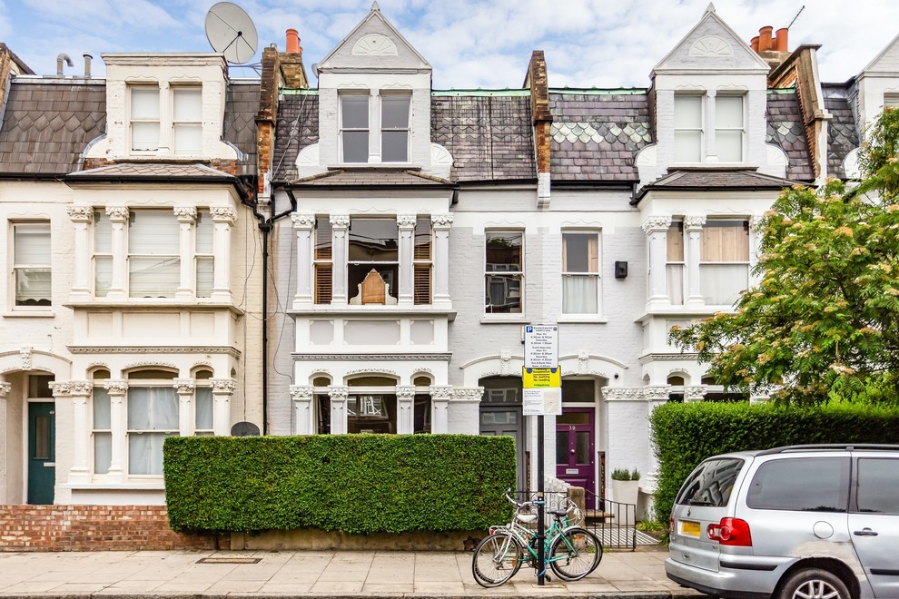Photo of a gey traditional terraced house in London with three floors and a shingle roof.