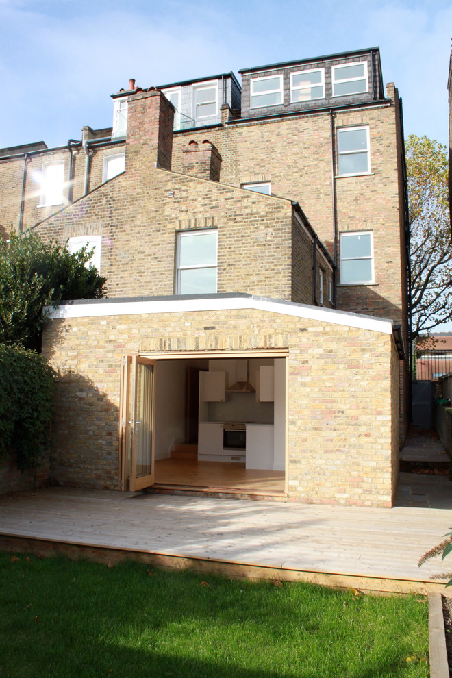 This is an example of a large and beige contemporary brick house exterior in London with three floors and a pitched roof.
