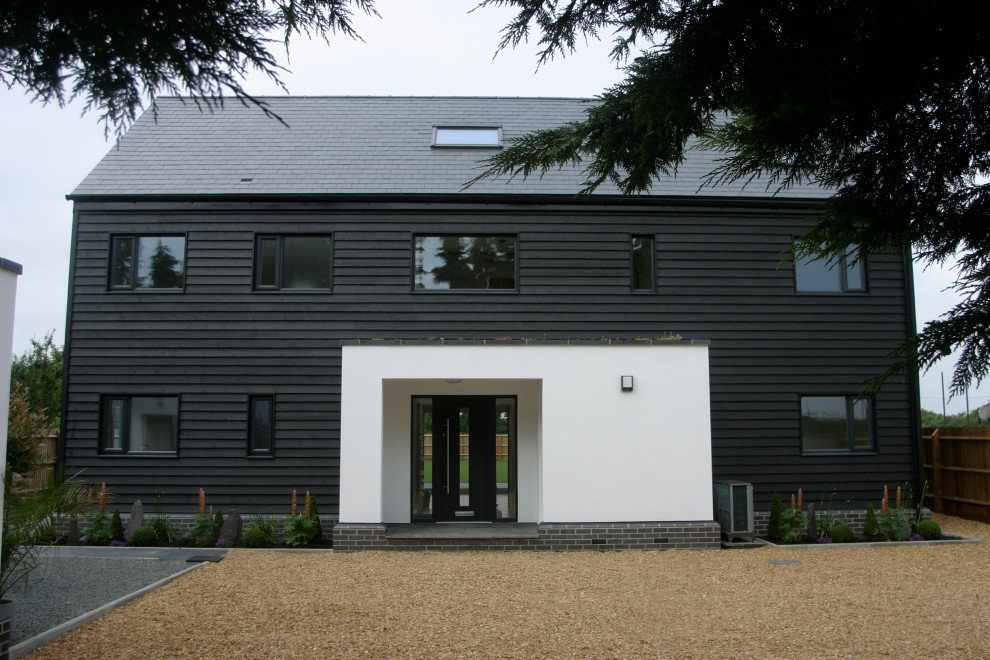 This is an example of a large and black contemporary detached house in Cambridgeshire with three floors, mixed cladding and a pitched roof.