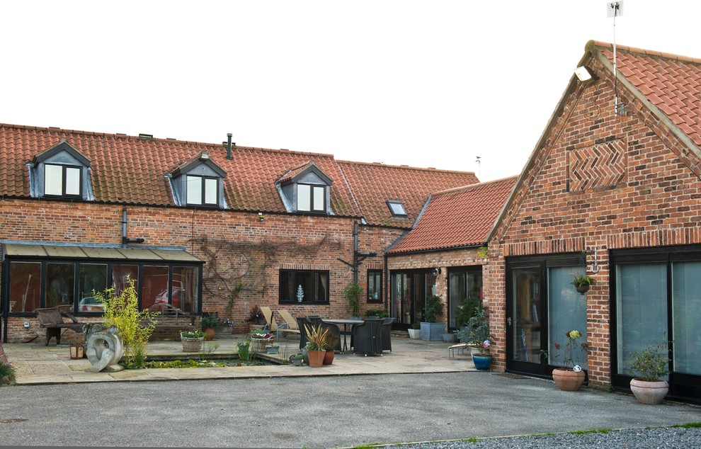 Aménagement d'une grande façade de maison marron campagne en brique à un étage avec un toit à deux pans.