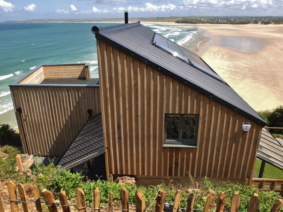 Exemple d'une façade de maison marron bord de mer en bois à un étage avec un toit en appentis et un toit en métal.