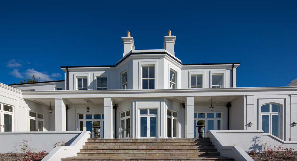 Immagine della villa ampia bianca classica a due piani con rivestimento in stucco, tetto a padiglione e copertura a scandole