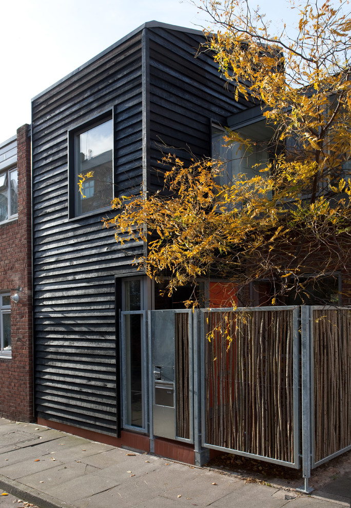 Стильный дизайн: маленький, двухэтажный, деревянный, черный таунхаус в современном стиле с двускатной крышей и металлической крышей для на участке и в саду - последний тренд