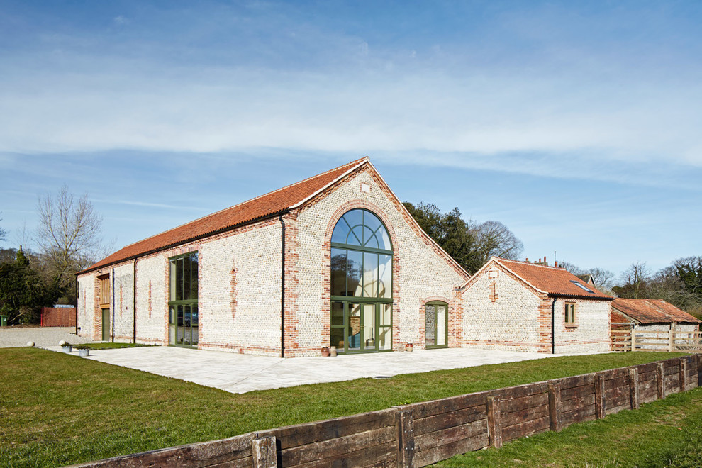 Cette image montre une grande façade de maison beige rustique en pierre de plain-pied avec un toit à deux pans et un toit en tuile.