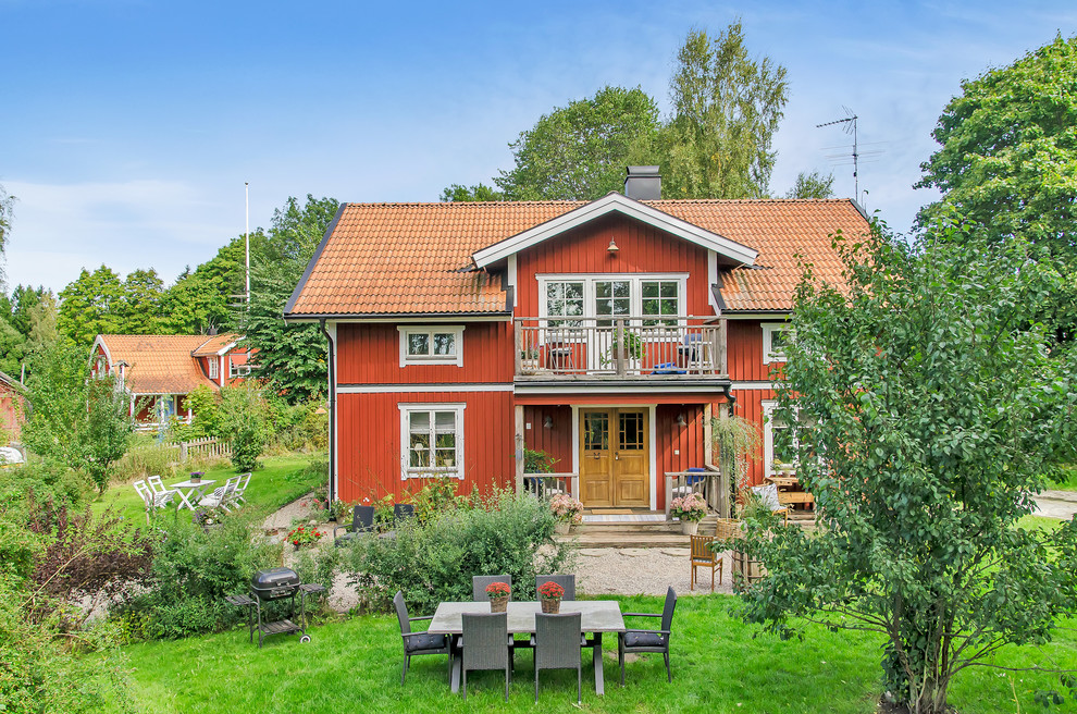 Inspiration for a medium sized and red rural two floor house exterior in Stockholm with wood cladding and a pitched roof.