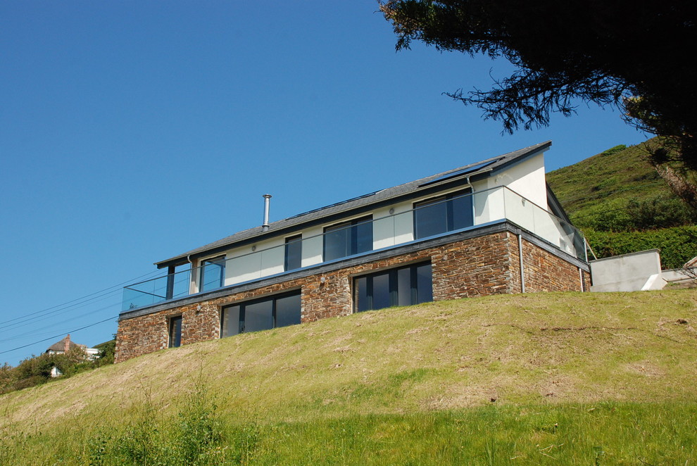 Imagen de fachada de casa blanca y gris actual de tamaño medio de dos plantas con revestimiento de piedra, tejado a dos aguas y tejado de teja de barro
