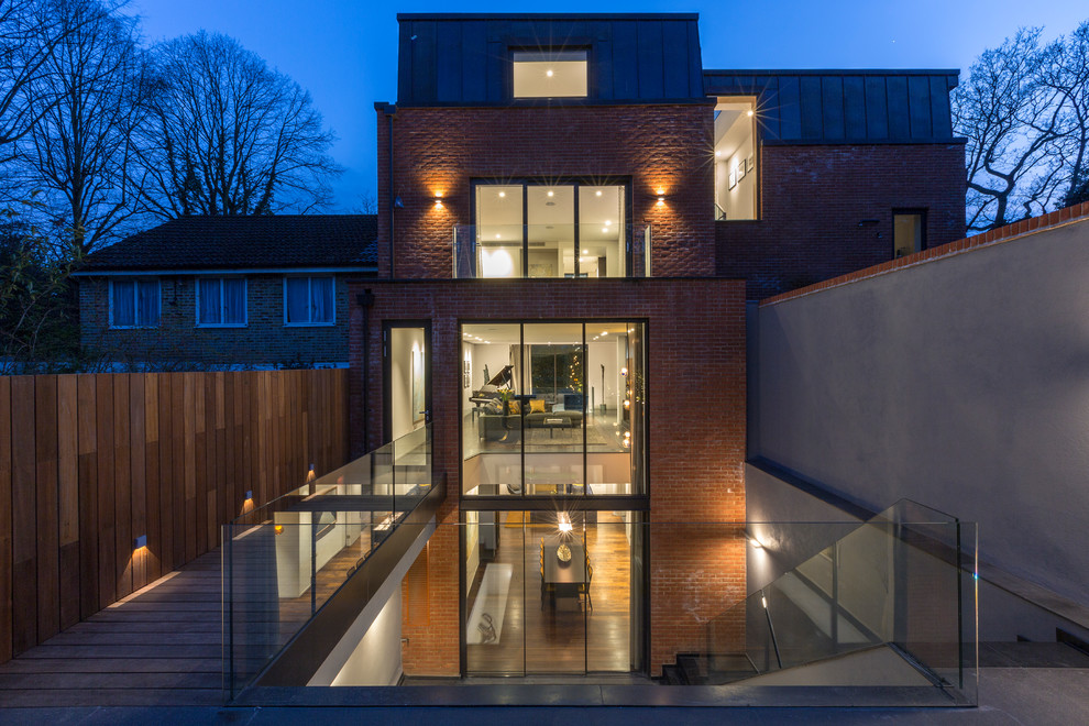 Photo of a medium sized and red contemporary brick semi-detached house in London with three floors and a flat roof.