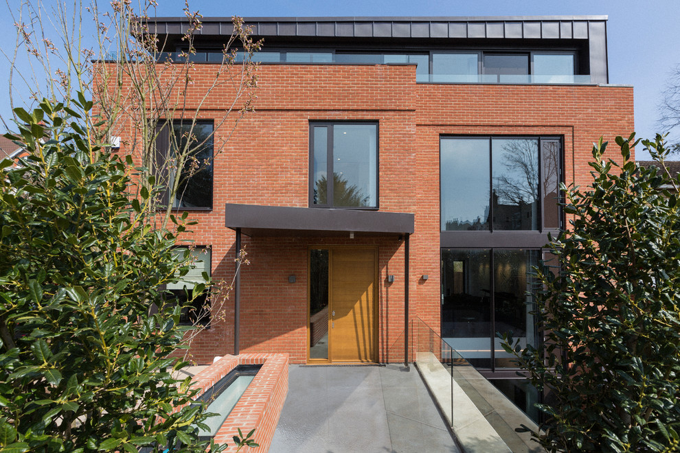 This is an example of a large and red contemporary brick detached house in London with three floors and a flat roof.