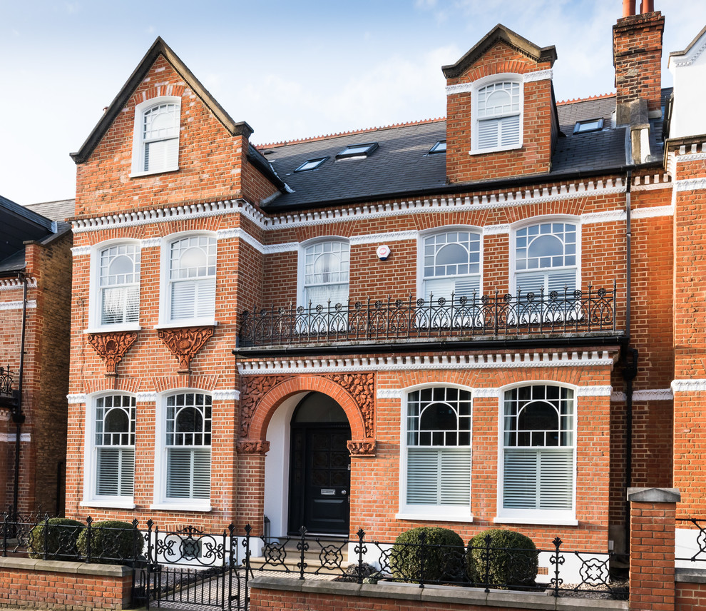 Red and expansive victorian brick semi-detached house in London with a pitched roof and three floors.