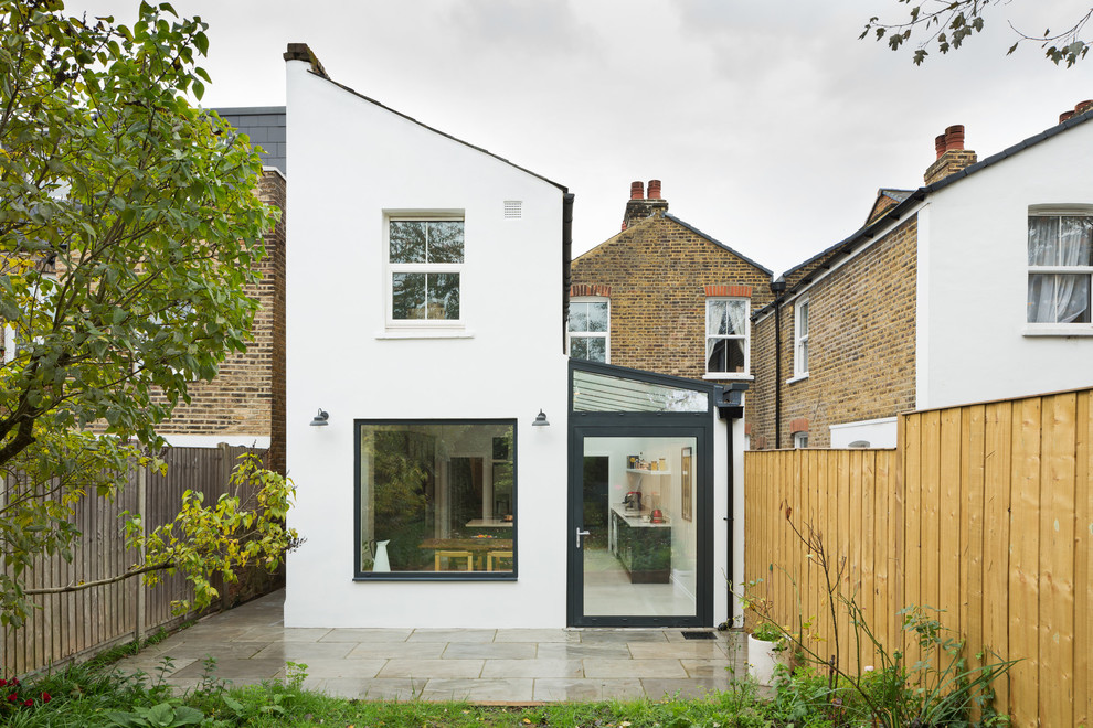 Trendy white two-story stucco house exterior photo in London with a shed roof and a shingle roof