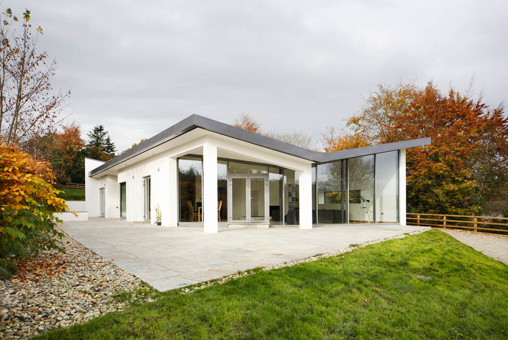 Cette image montre une façade de maison blanche minimaliste en stuc de plain-pied avec un toit plat.