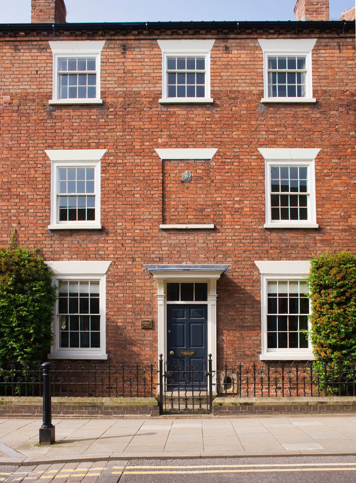 This is an example of a red classic brick terraced house in Other with three floors and a flat roof.