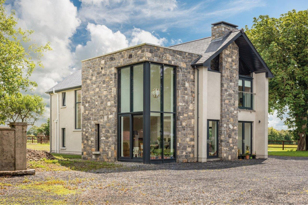 Inspiration pour une grande façade de maison grise minimaliste en pierre à un étage avec un toit à deux pans et un toit en tuile.