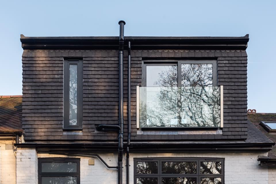 Large modern black three-story mixed siding townhouse exterior idea in London with a hip roof, a tile roof and a black roof