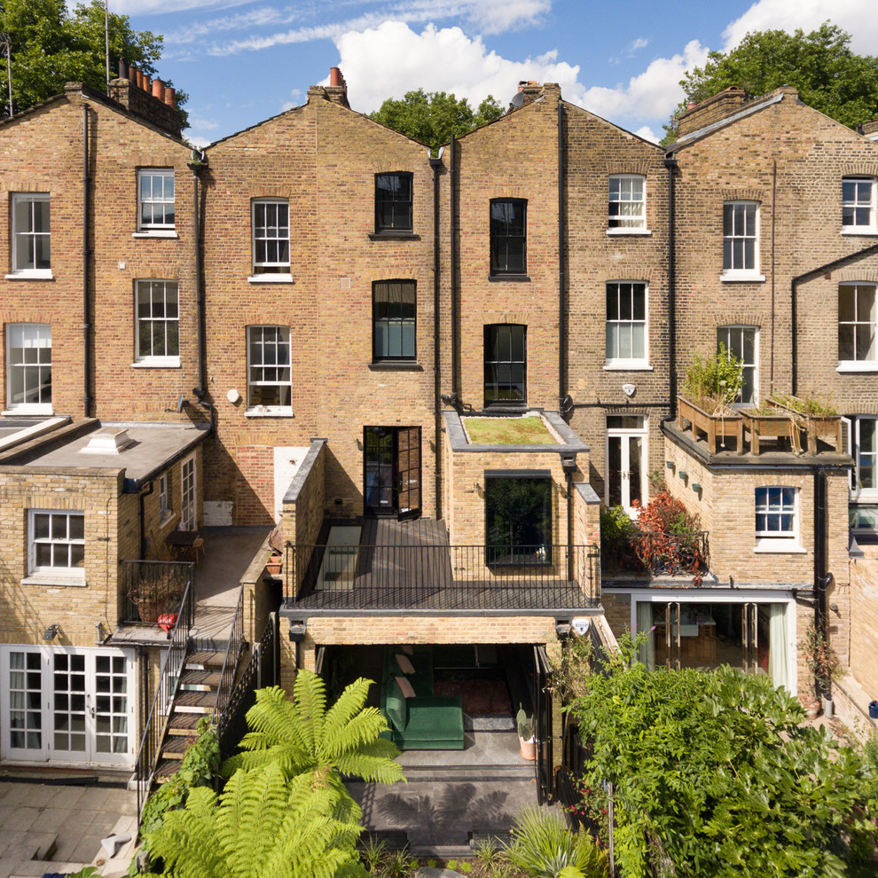 Large and yellow contemporary brick terraced house in London with three floors, a pitched roof and a tiled roof.