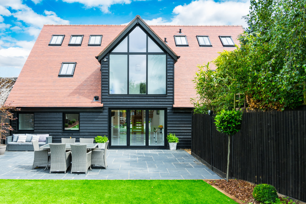 Large trendy black two-story wood exterior home photo in Hertfordshire with a tile roof