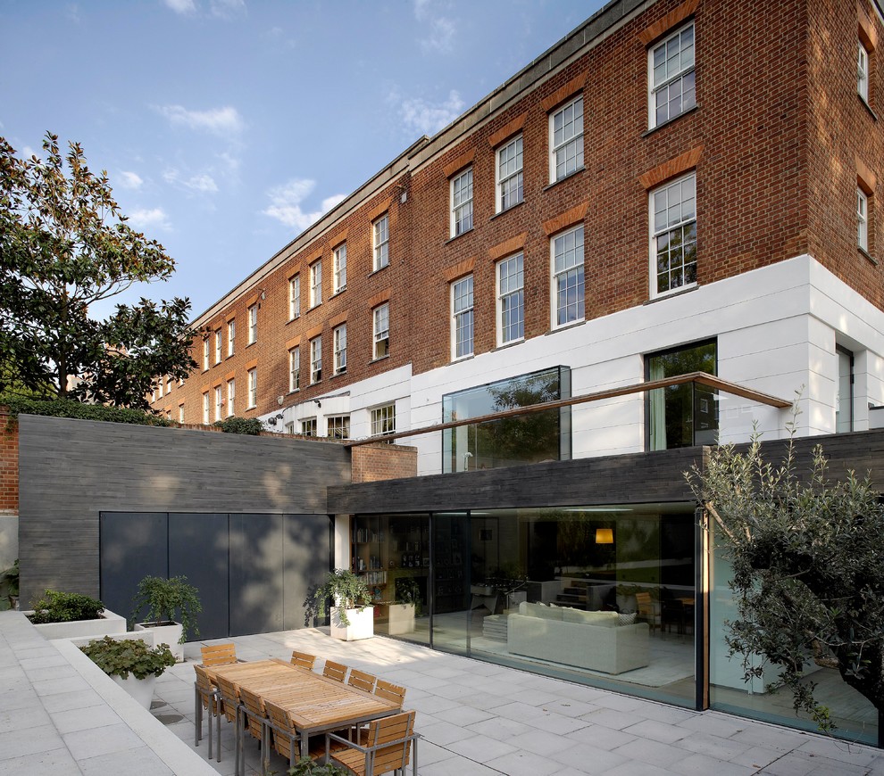 This is an example of a large and gey contemporary house exterior in London with three floors, stone cladding and a flat roof.