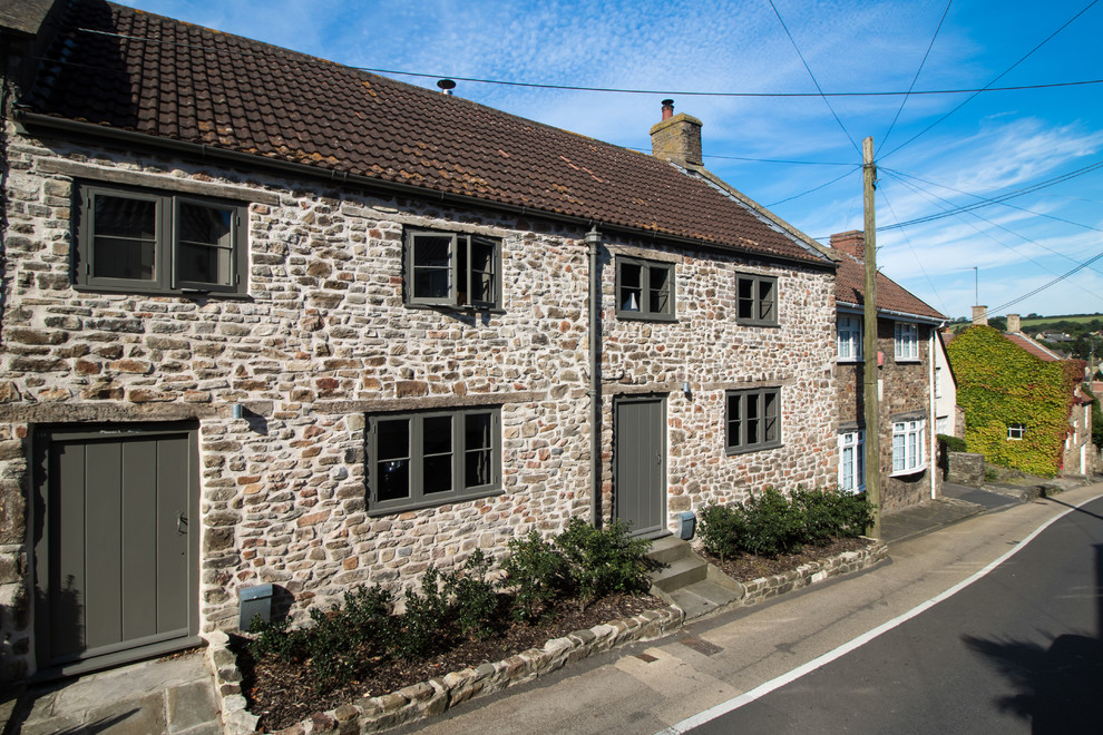 Small and brown two floor house exterior in Other with stone cladding and a pitched roof.