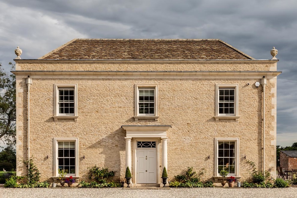 Beige classic detached house in Gloucestershire with stone cladding and a pitched roof.