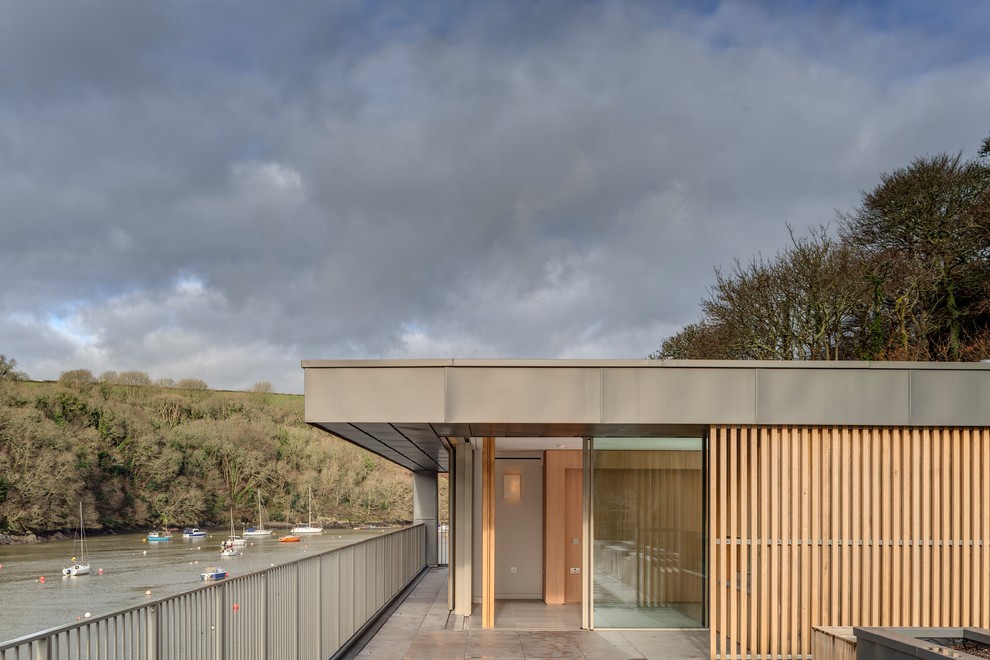 Photo of a brown modern two floor detached house in Devon with wood cladding, a flat roof and a mixed material roof.