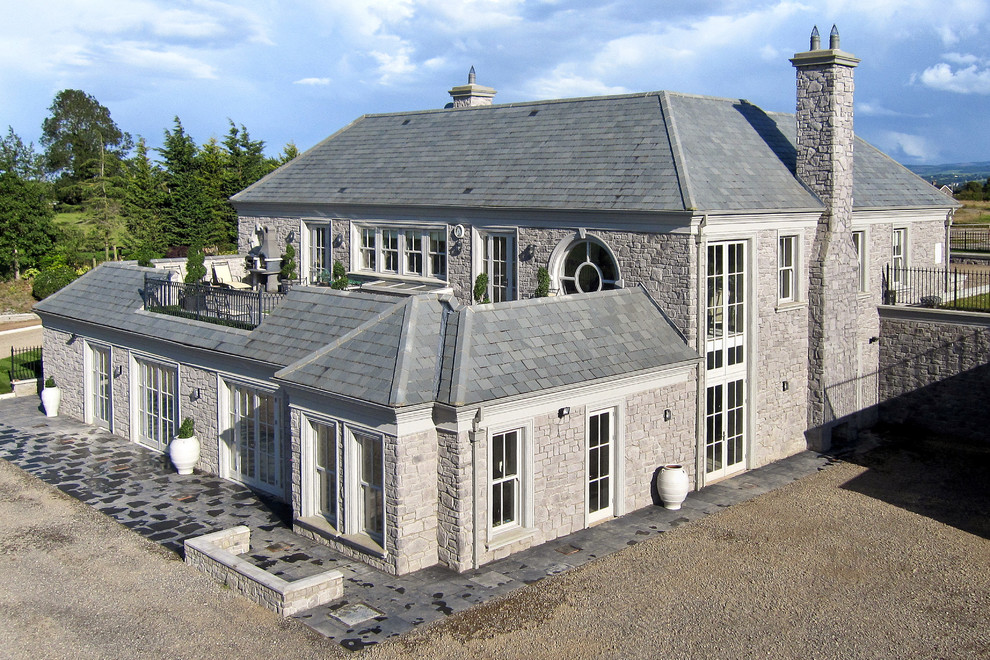 Foto della villa grigia classica a due piani di medie dimensioni con rivestimento in pietra, tetto a padiglione e copertura a scandole