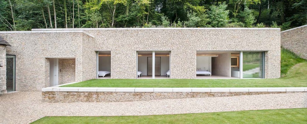 Ispirazione per la facciata di una casa beige moderna con rivestimento in pietra e terreno in pendenza