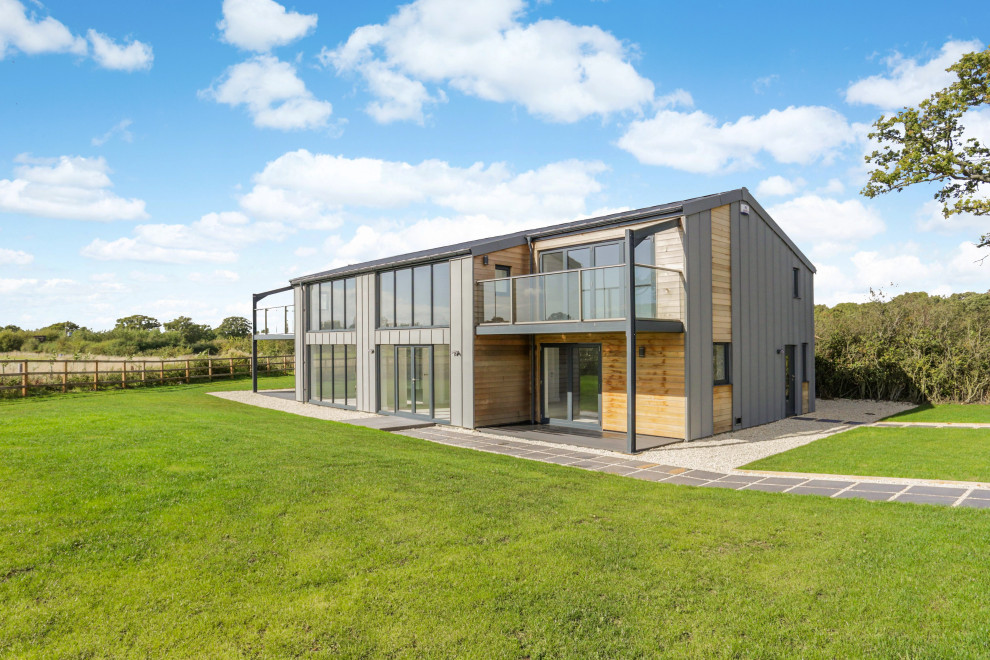 This is an example of a large and gey modern two floor detached house in Wiltshire with metal cladding, a pitched roof and a metal roof.