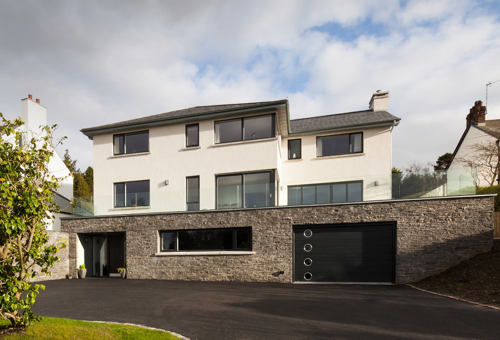 This is an example of an expansive and white contemporary house exterior in Belfast with three floors, stone cladding and a pitched roof.