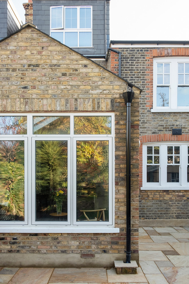 Example of a mid-sized classic two-story brick duplex exterior design in London with a hip roof and a shingle roof