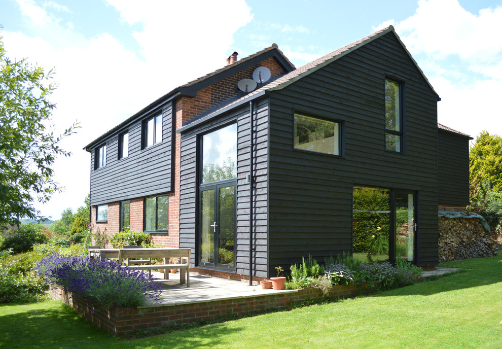 Medium sized and black contemporary two floor house exterior in Surrey with wood cladding.