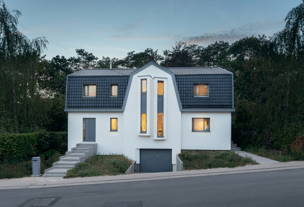 Стильный дизайн: двухэтажный, белый частный загородный дом среднего размера в скандинавском стиле с облицовкой из цементной штукатурки, мансардной крышей и черепичной крышей - последний тренд