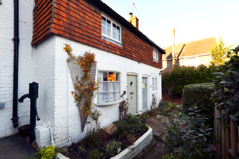 Small and white farmhouse two floor house exterior in Sussex with mixed cladding and a pitched roof.