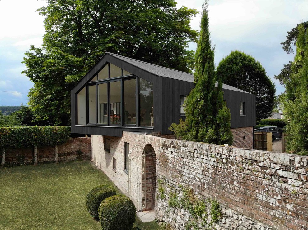 На фото: маленький, двухэтажный, черный частный загородный дом в современном стиле с комбинированной облицовкой и двускатной крышей для на участке и в саду