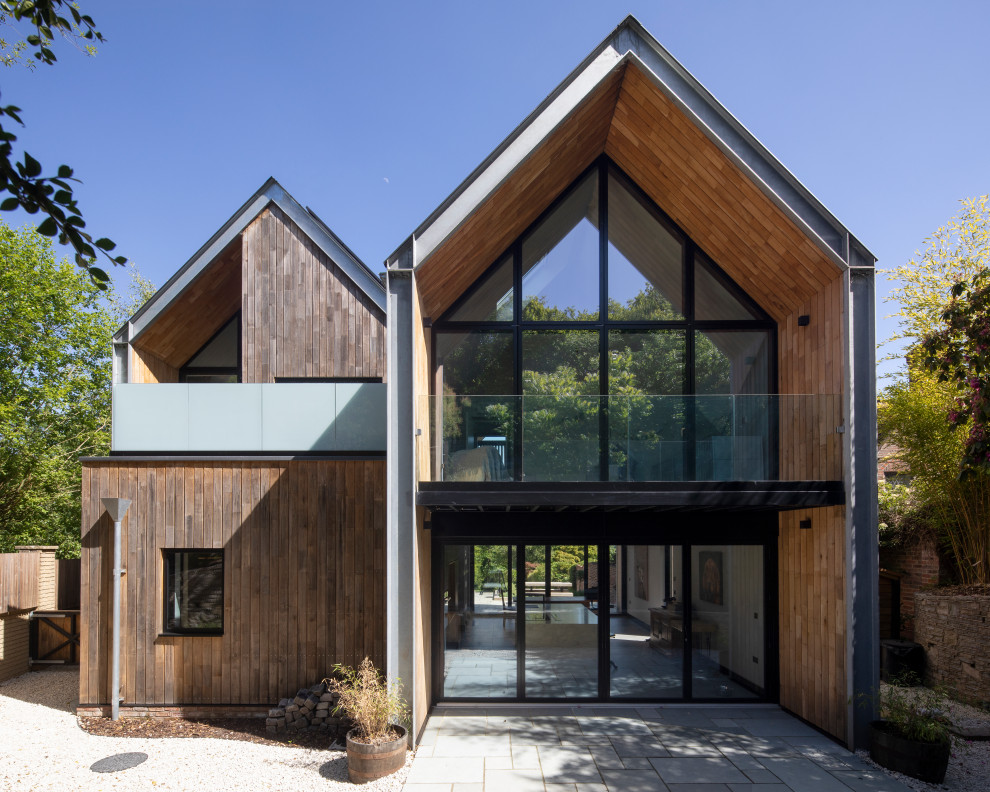 This is an example of a large contemporary two floor house exterior in Hampshire with wood cladding, a pitched roof and a metal roof.