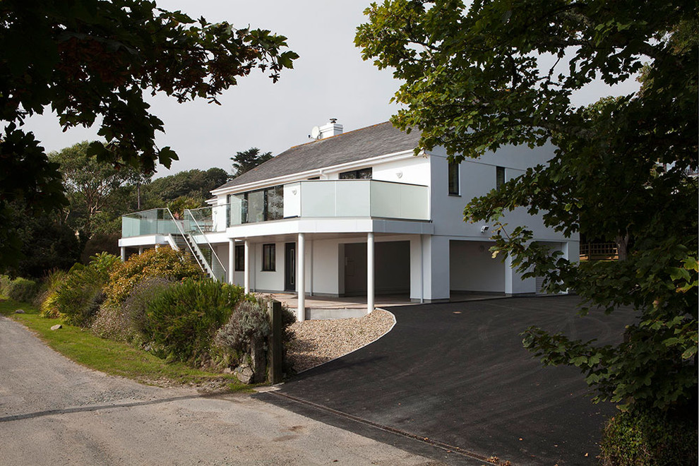 На фото: маленький, двухэтажный, белый дом в современном стиле с облицовкой из цементной штукатурки и двускатной крышей для на участке и в саду