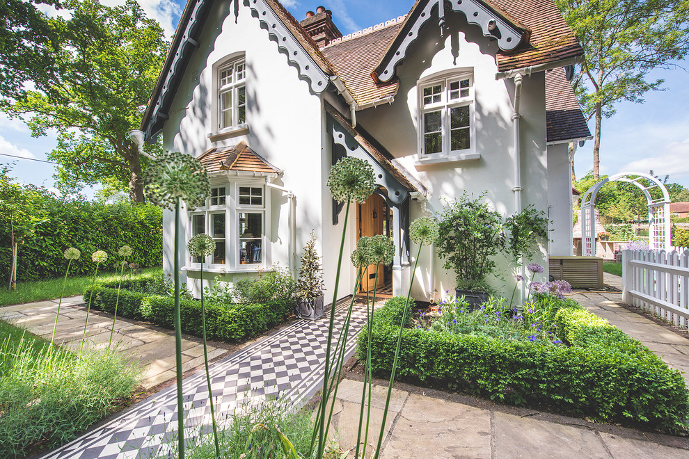 На фото: маленький, двухэтажный, белый дом в классическом стиле с облицовкой из цементной штукатурки и двускатной крышей для на участке и в саду