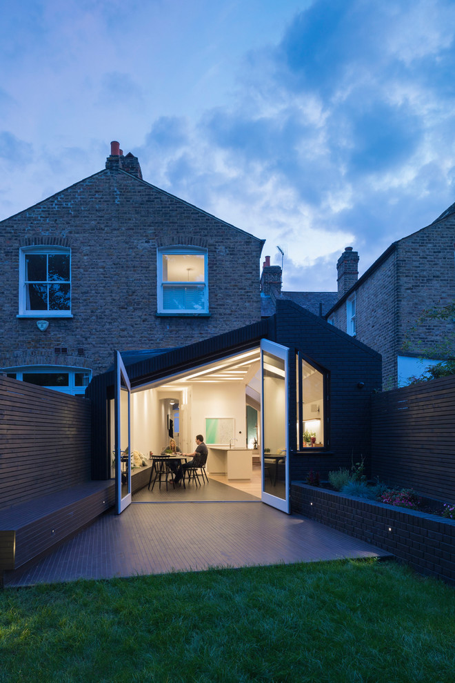 Cette image montre une façade de maison noire design en brique de plain-pied avec un toit à deux pans et un toit mixte.