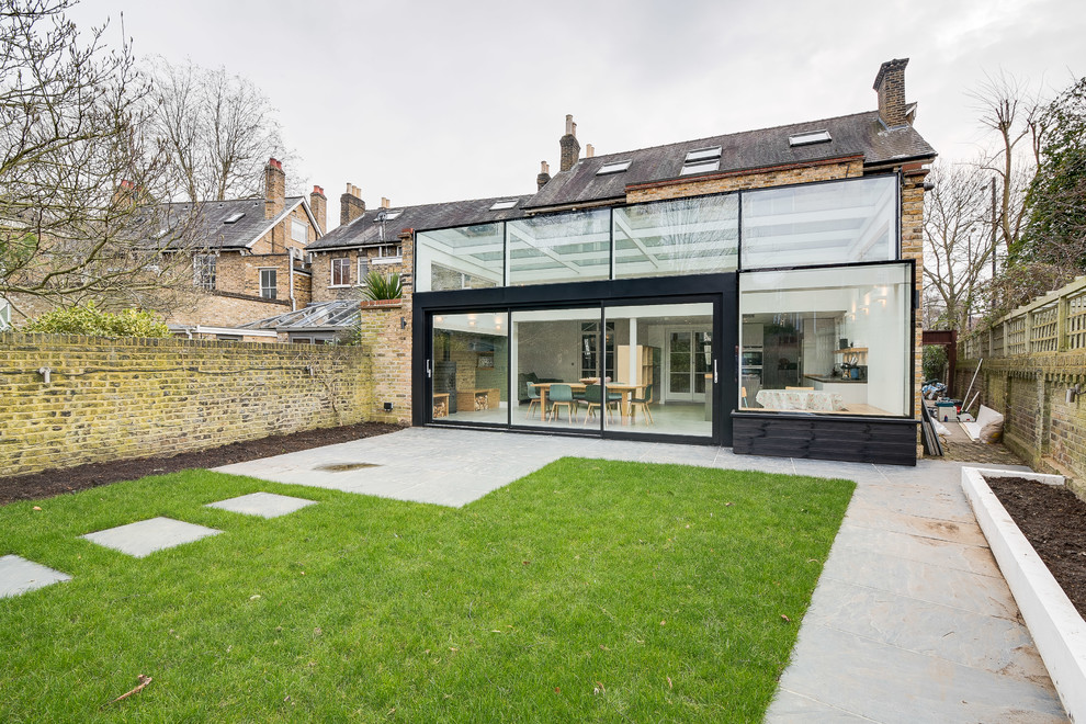 Large and black contemporary detached house in London with three floors, wood cladding, a flat roof and a mixed material roof.