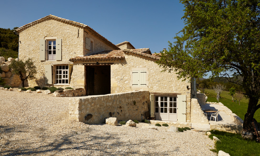 Immagine della facciata di una casa grande beige mediterranea a due piani con rivestimento in pietra e tetto a capanna