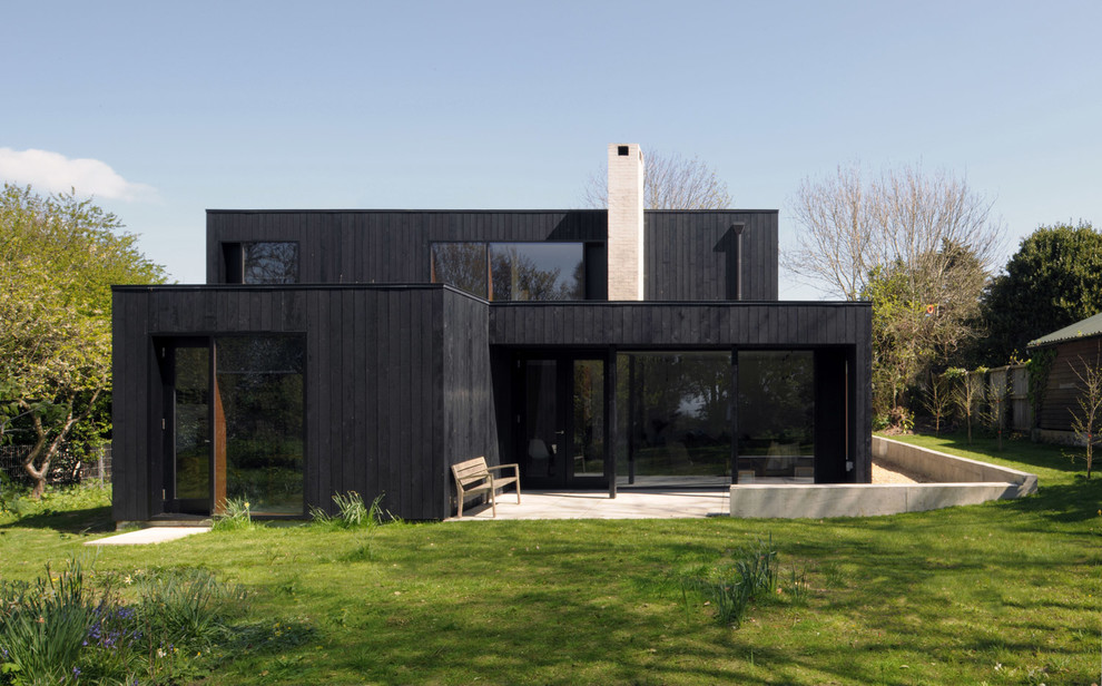 Foto della villa nera contemporanea a due piani con rivestimento in legno e tetto piano